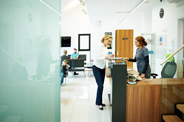 Mature female patient at dental clinic Mature woman standing at the reception desk in a dental clinic filling out the papers medical clinic stock pictures, royalty-free photos & images