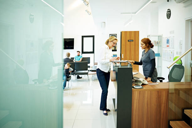 Mature female patient at dental clinic Mature woman standing at the reception desk in a dental clinic filling out the papers medical office lobby stock pictures, royalty-free photos & images