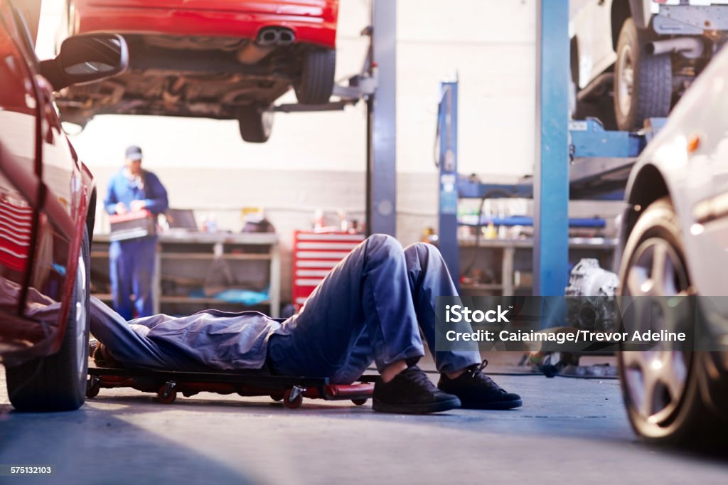Mechanic under car in auto repair shop  Car Stock Photo