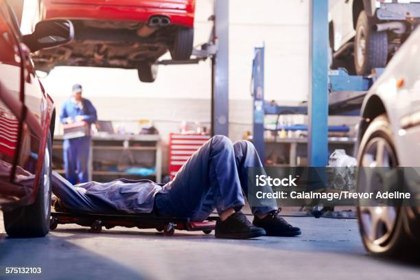 Mechanic Under Car In Auto Repair Shop Stock Photo - Download Image Now - Car, Auto Repair Shop, Mechanic