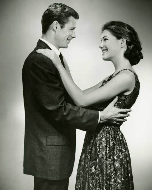 giovane coppia standing faccia a faccia, sorridente, in studio (b & w - 1950s style couple old fashioned heterosexual couple foto e immagini stock