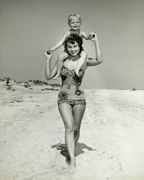 Mother carrying son (2-3) on shoulders, walking on beach, (B&W), portrait  one piece swimsuit photos stock pictures, royalty-free photos & images