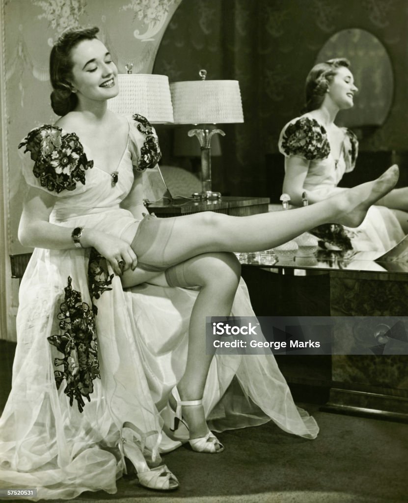 Glamorous woman in evening gown putting on silk stockings, (B&W)  1940-1949 Stock Photo