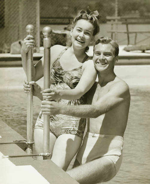Couple standing at railings in pool, (B&W), portrait  one piece swimsuit photos stock pictures, royalty-free photos & images