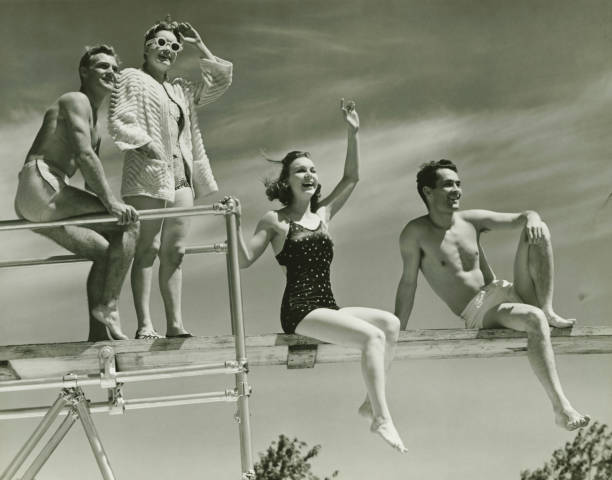 Two couples on springboard, (B&W), low angle view  one piece swimsuit photos stock pictures, royalty-free photos & images