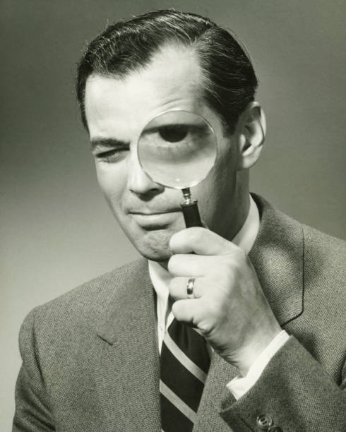 businessman in full suit in studio looking through magnifying glass, (b&w), portrait - 舊式 圖片 個照片及圖片檔