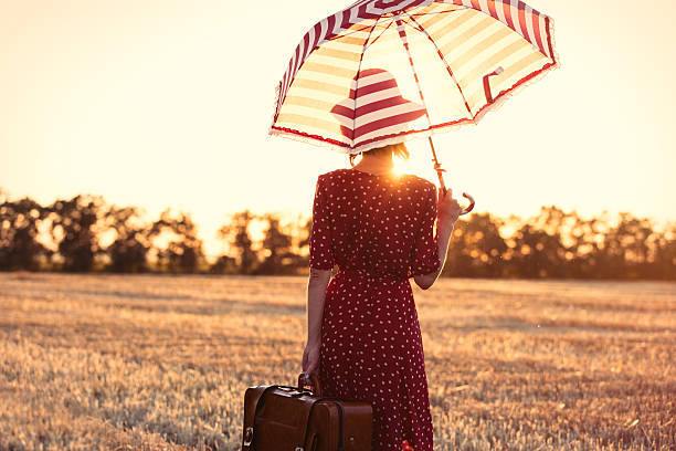 photo of the beautiful young woman with red umbrella and brown suitcase standing in the field