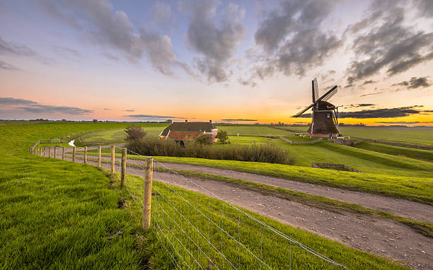 Dutch Wooden windmill in flat grassy landscape Ultra wide angle scene of Dutch Wooden windmill in flat grassy landscape under beautiful sunset seen from the sea dike at Waddensea, Netherlands friesland netherlands stock pictures, royalty-free photos & images