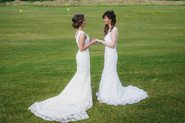 Two beautiful brides holding hands on the green field of the golf club