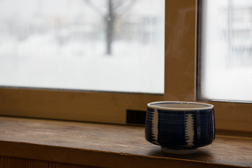 Hot Japan tea cup on wood bar beside window at snowy day, Hakkaido, Japan