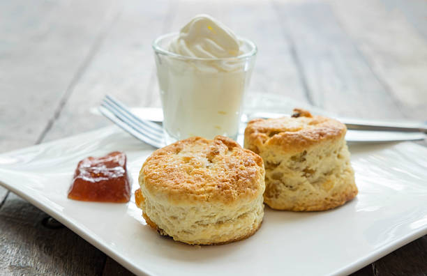 Scones with cream and jam in white plate on wooden desk