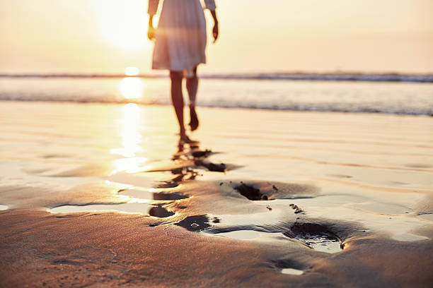 istock Footprints in sand with woman walking in background during sunse 576573164
