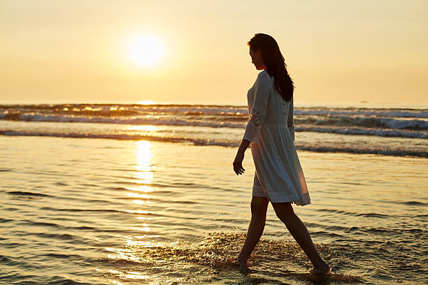 istock Woman walking on water's edge during sunset 576574318