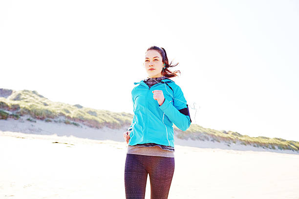 istock Sporty woman running on beach against clear sky 576576680