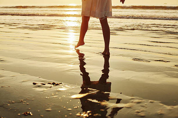 istock Low section of woman walking barefoot on shore during sunset 576577096