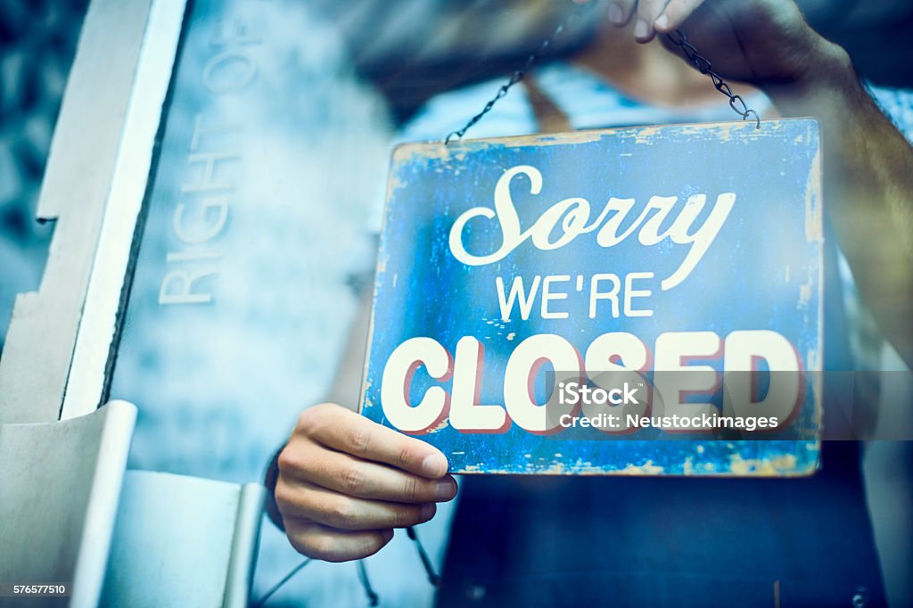 Waiter hanging closed sign on glass window Midsection of waiter hanging closed sign on window. Low angle view of text is seen through glass. Young barista is standing in coffee shop. Closed Sign Stock Photo