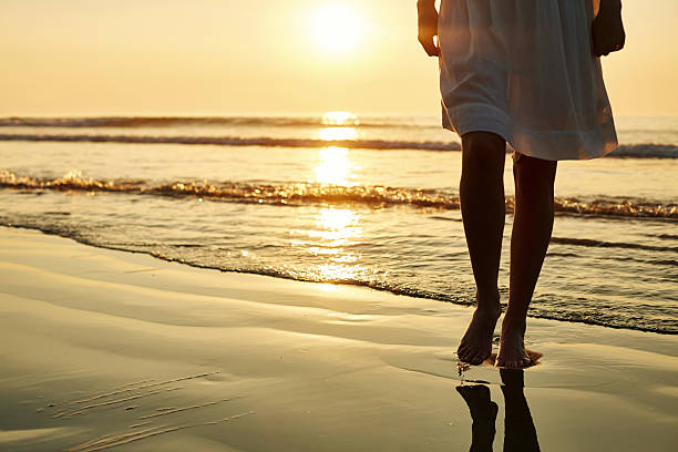 istock Woman walking barefoot on wet shore during sunset 576577740