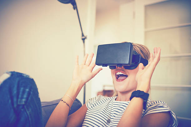 istock Excited young woman using virtual reality headset at home 576577992