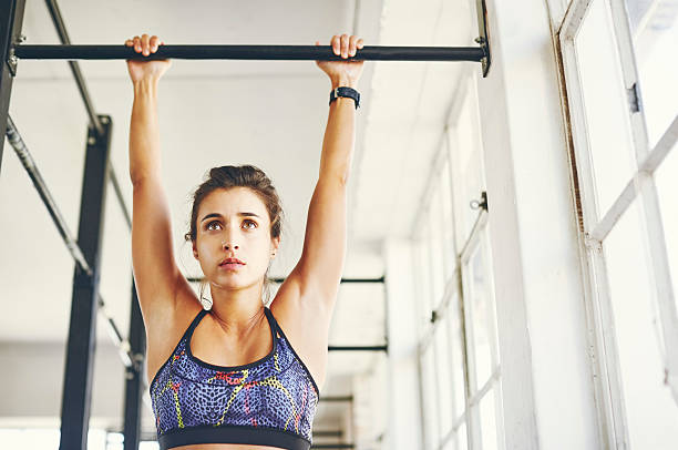 Low angle view of young female doing chin-ups Low angle view of female doing chin-ups in gym. Young woman is exercising on gymnastics bar. She is wearing sports clothing. chin ups photos stock pictures, royalty-free photos & images