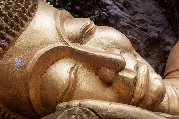Head of a reclining golden concrete Buddha in a park in Luang Prabang, the former capital of Laos.
