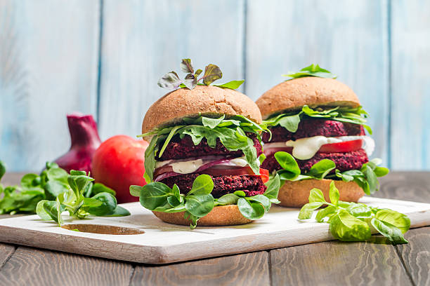 Vegetarian burger made of beetroot Vegetarian burger made of beetroot, tomato, corn salad and arugula on wooden background veggie burger photos stock pictures, royalty-free photos & images