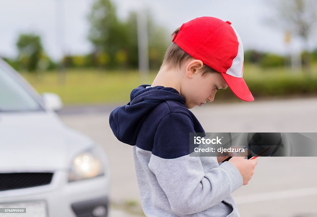 Child playing mobile games on smartphone on the street Child busy playing the smartphone mobile games does not pay attention to the moving car. Boy child playing mobile games on smartphone on the street Child Stock Photo