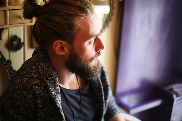 Young worried Caucasian man with beard and ponytail indoor.