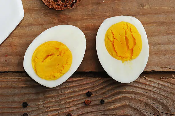 Photo of two halves of boiled eggs on wooden rustic background