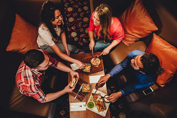 Overhead view of a group of friends having a meal at a restaurant. They are eating burgers and fish with chips.
