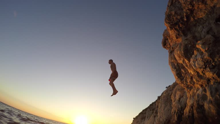 POV A person in the water watching a friend jump off a cliff at sunset