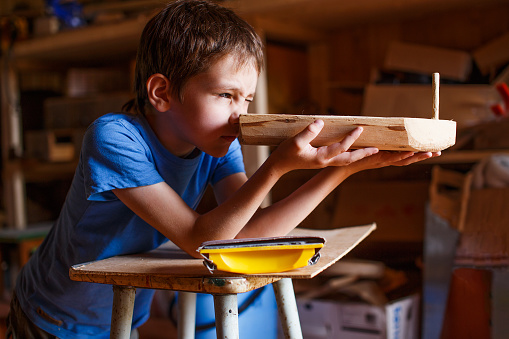 child in the workshop makes crafts. toy boat of wood