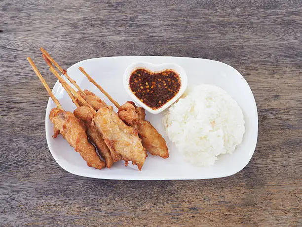Fried chicken skewers with spicy sauce and sticky rice on white plate. Thai food style.