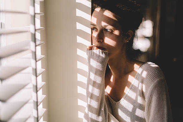 triste femme regardant par la fenêtre - women depression window sadness photos et images de collection