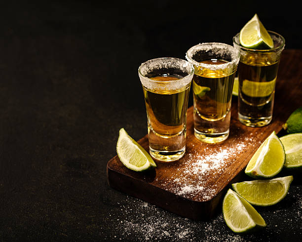 Mexican Gold Tequila with lime and salt on wooden table Mexican Gold Tequila with lime and salt on wooden table, selective focus. Copyspace. shot glass stock pictures, royalty-free photos & images