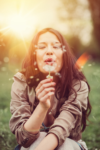 Young woman blowing dandelions among nature