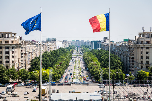 Romanian and European Union (EU) flag flying in Bucharest, Romania. In the background cars are driving down one of the busiest avenues in Bucharest, the capital city of Romania. Horizontal colour image with room for copy space.