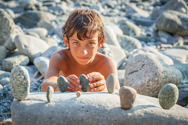Young boy carefully piling stones into a balanced stack while playing on the beach during a sunny day.