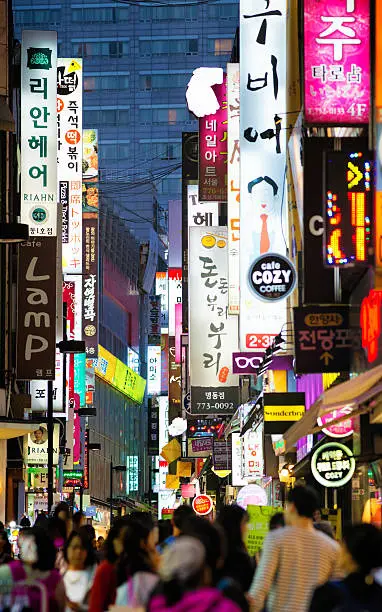 Seoul shopping Myeongdong street at night with a crowd of customers and layers of neon and illuminated advertisement.