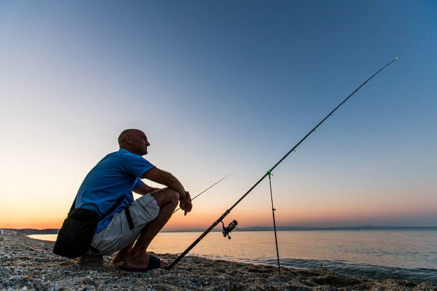 A man crouching on the beach while fishing