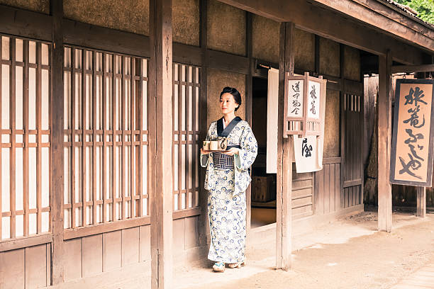 Japanese woman with tea tray outside a traditional japanese house Retro revival image of a geisha walking in front of her house.  She's wearing a traditional kimono and brings a tea tray with tea mugs and teapot. Kyoto - Japan traditional ceremony photos stock pictures, royalty-free photos & images