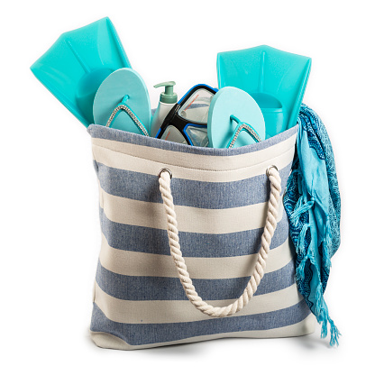 Nicely isolated on a pure white background, the beach bag contains several items, such as fins, sandals, goggle and sarong. In a duotone mode based on blue and white tones, studio shot and professionally isolated.