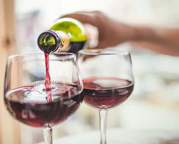 Unrecognizable man pouring red wine in two glasses.