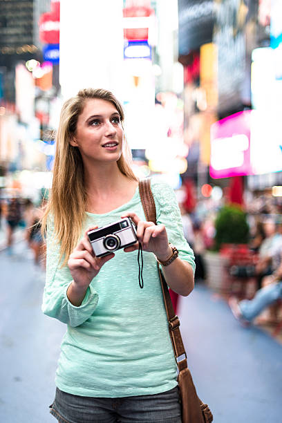 istock pretty woman smiling on times square with camera 576748270