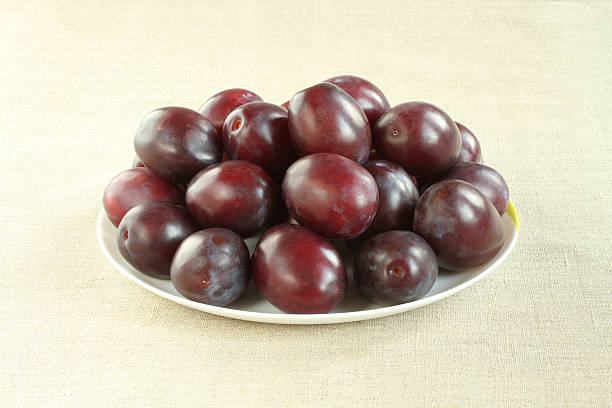istock Ripe purple plums on white plate on linen cloth. Closeup 576750106