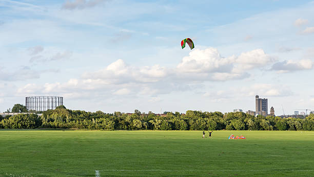 Kite flying on Wormwood Scrubs London, England - July 10, 2016: Two people fly a large kite on Wormwood Scrubs common in west London, with the Trellick Tower and housing blocks of North Kensington behind. trellick tower stock pictures, royalty-free photos & images