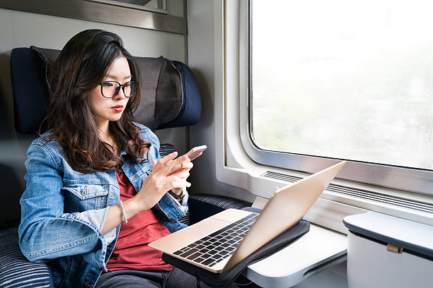 nette asiatische frau mit smartphone und laptop im zug - japanese ethnicity train women asian ethnicity stock-fotos und bilder