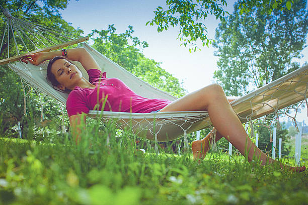 junge sorglos frau entspannt sich in einer hängematte im garten - formal garden flower bed women grass stock-fotos und bilder