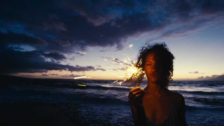 Beautiful young woman walking with sparkler fireworks on the beach at twilight