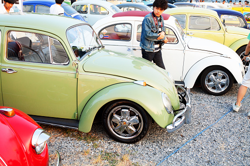 Bangkok, Thailand - February 15, 2014: Some thai men are walking between row pf parked VW Beetle oldtimers at Siam VW festival. Annual public oldtimer meeting. Man in center has a camera.