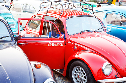 Bangkok, Thailand - February 15, 2014: Thai man is sitting in a red VW Beetle Volkswagen oldtimer. Oldtimer is parked in a rows of man Beetle oldtimers on public Siam VW festival at Fashion Island. In background some men are walking between cars.